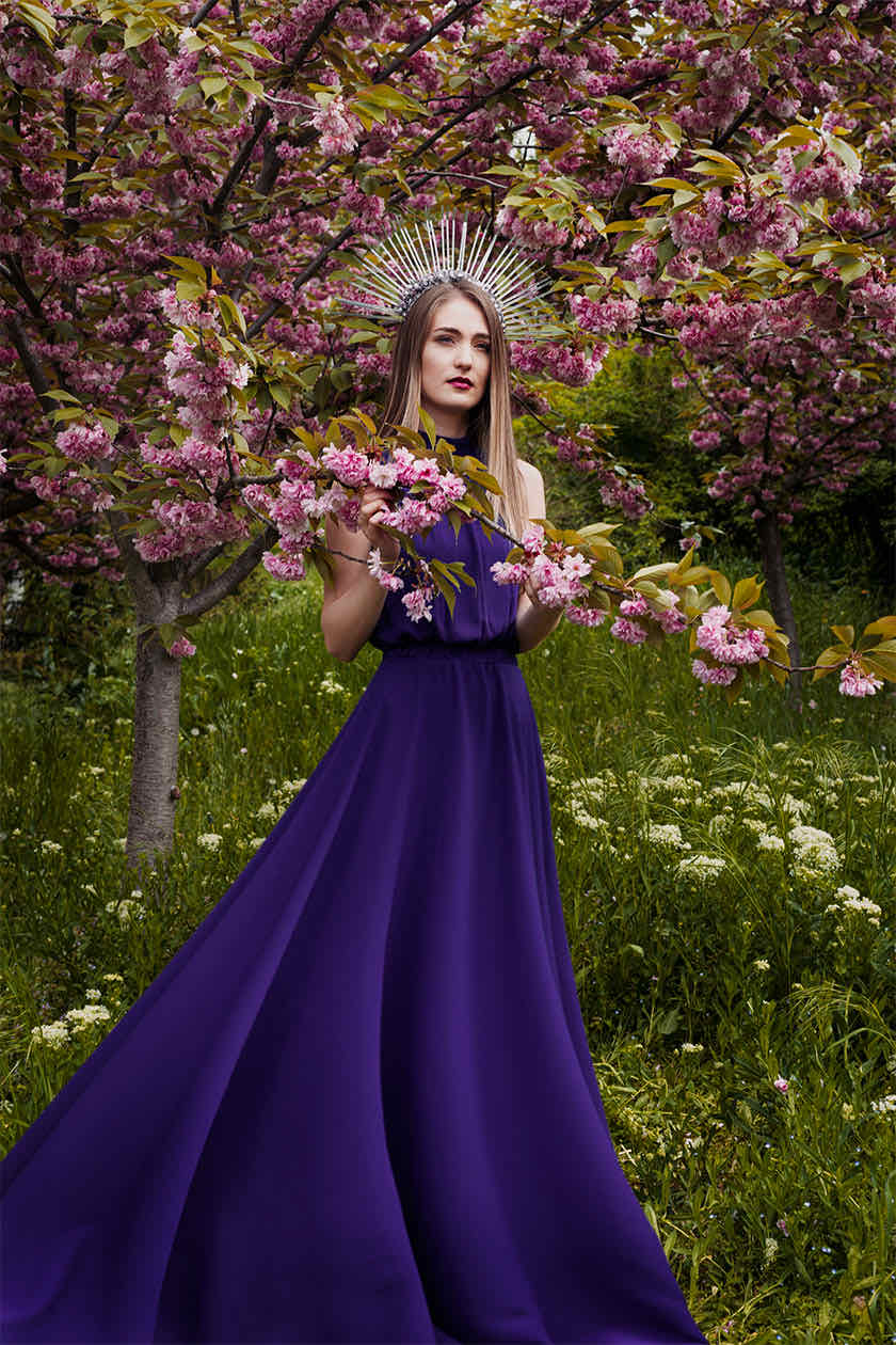 Woman in a deep purple gown and silver spiked crown, holding a flowering cherry blossom branch